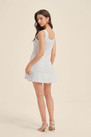Back view of a woman wearing a blue jacquard floral mini dress with wide straps and a subtle flare skirt, styled with heels.
