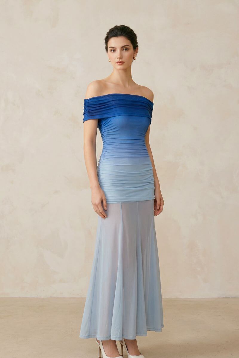 A model poses in a blue ombre off-shoulder mesh maxi dress highlighting the ruched waist and fluid sheer hem, captured from a soft angled studio view.