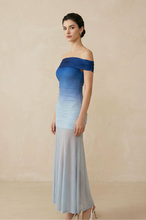 Side view of a blue gradient off-shoulder mesh maxi dress showing a slim fitted silhouette and lightweight sheer skirt, styled in a neutral studio environment.