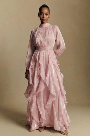 A model stands facing forward wearing a blush pink chiffon maxi dress featuring a gathered high neck, cinched waist, and cascading ruffle layers for an elegant silhouette.