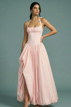 A side view of a model wearing a blush pink halter corset maxi dress highlights the sculpted waist, airy skirt volume, and elegant proportions in a clean studio environment.