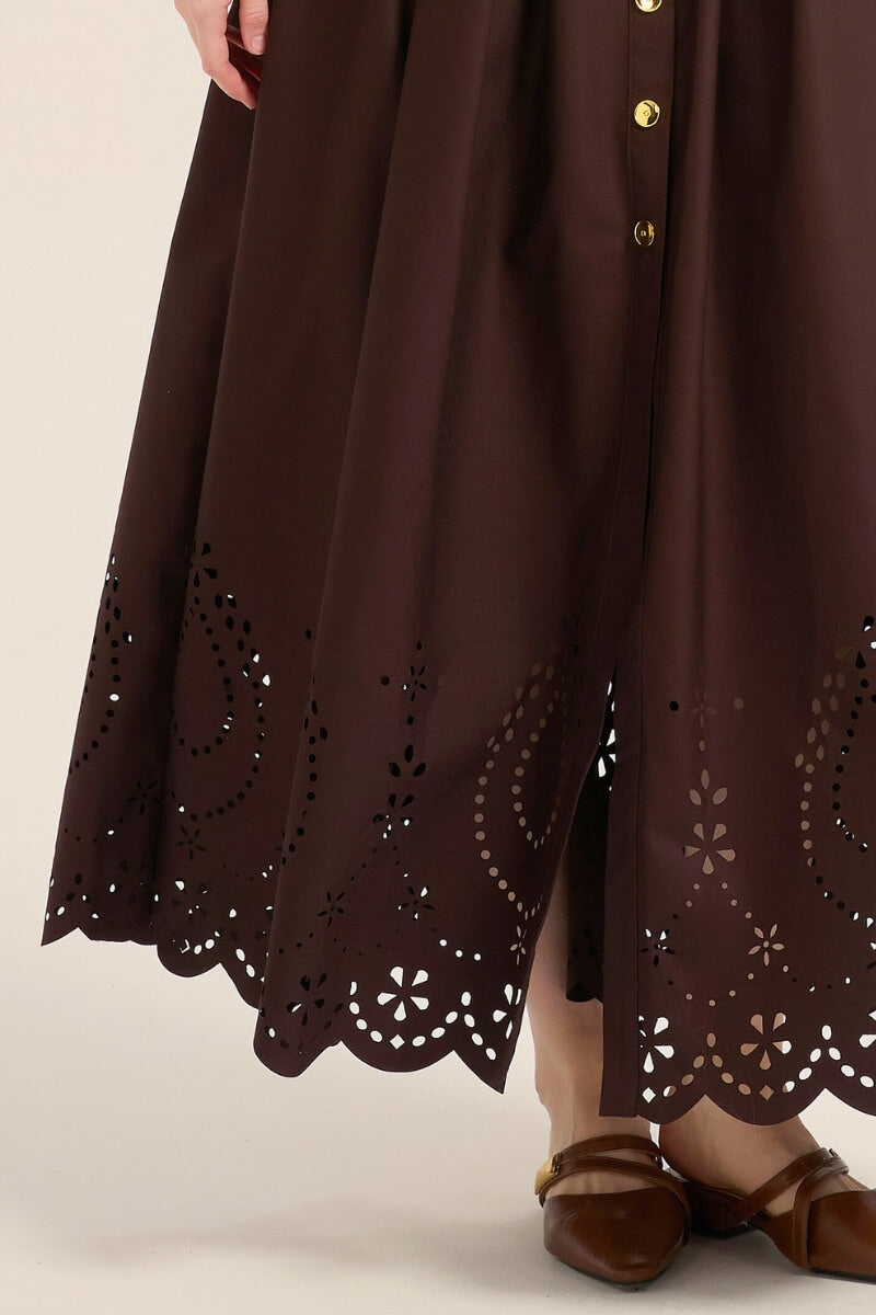 Close-up of the lower skirt showing intricate floral eyelet cutouts and scalloped hem design on a brown cotton maxi dress.