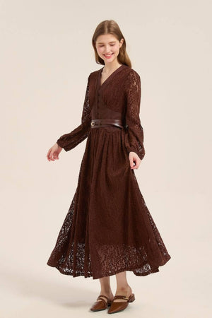 Model walking gracefully in a brown lace maxi dress featuring a V-neckline, long sleeves, and a wide leather belt accentuating the waist.