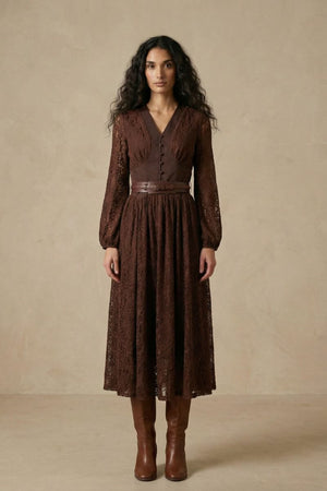 A woman wearing a brown lace long-sleeve midi dress featuring a V-neck bodice, fitted waist with a leather belt, and a softly flared lace skirt.