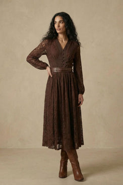 A woman wearing a brown lace long-sleeve midi dress featuring a V-neck bodice, fitted waist with a leather belt, and a softly flared lace skirt.