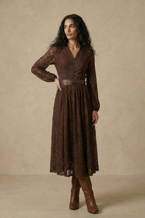 A woman wearing a brown lace long-sleeve midi dress featuring a V-neck bodice, fitted waist with a leather belt, and a softly flared lace skirt.