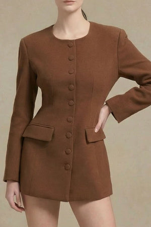 Model standing confidently in a brown structured blazer mini dress with fabric-covered buttons and a fitted silhouette, styled with knee-high embossed brown boots against a minimal background.