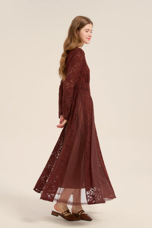 Model walking sideways in a burgundy lace and mesh long sleeve maxi dress with flowing skirt and layered lace texture.