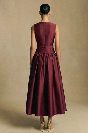 Back view of a burgundy sleeveless midi dress showing a clean tailored back, concealed zipper, cinched waist, and flowing skirt with soft structure.