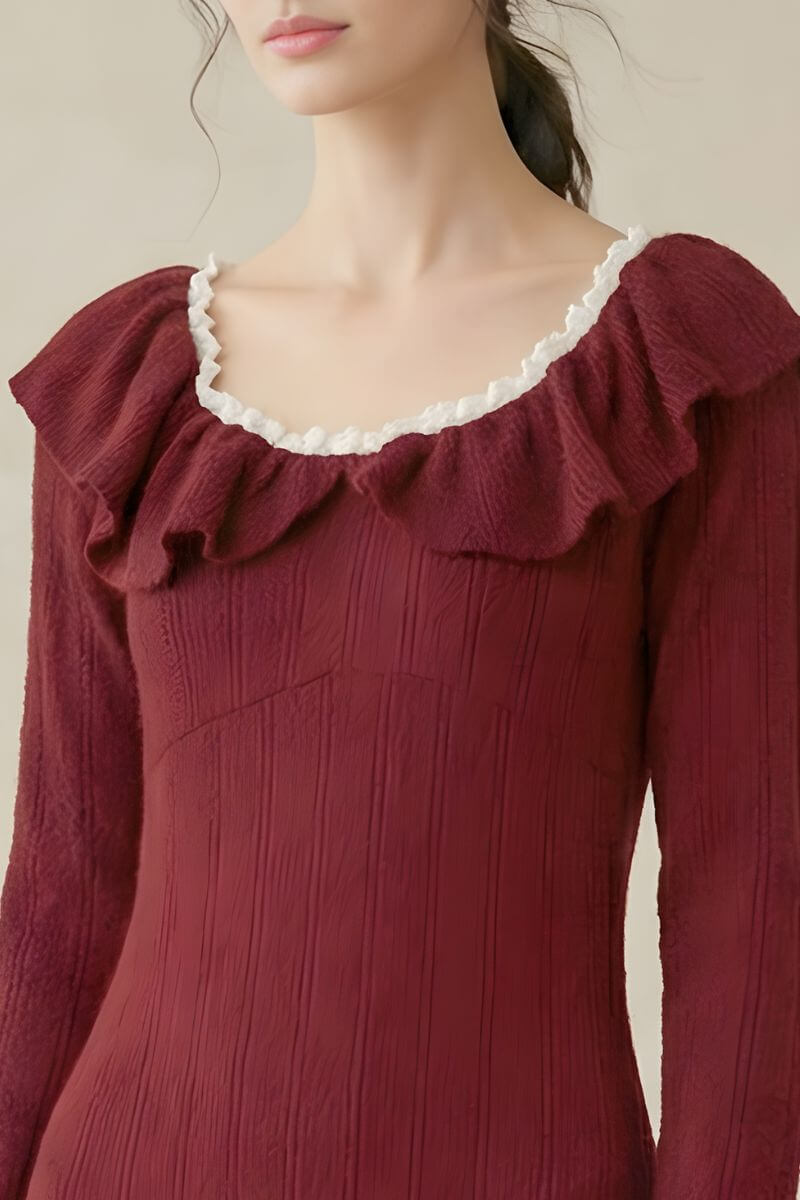 A close-up view of a burgundy textured knit dress showing the ruffled neckline with cream trim and long-sleeve detailing.