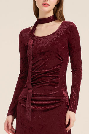 Close-up of the burgundy velvet dress showing its scoop neckline and attached scarf tie accent, highlighting the rich crushed velvet texture.