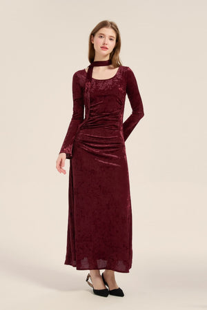 Full-length view of a model in a burgundy velvet maxi dress with long sleeves and ruched waist, paired with black pointed-toe heels.