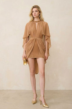 Model wearing a camel chiffon mini dress with sculpted draping and cape-like sleeves, styled for an evening occasion with gold accessories and a minimalist neutral backdrop.