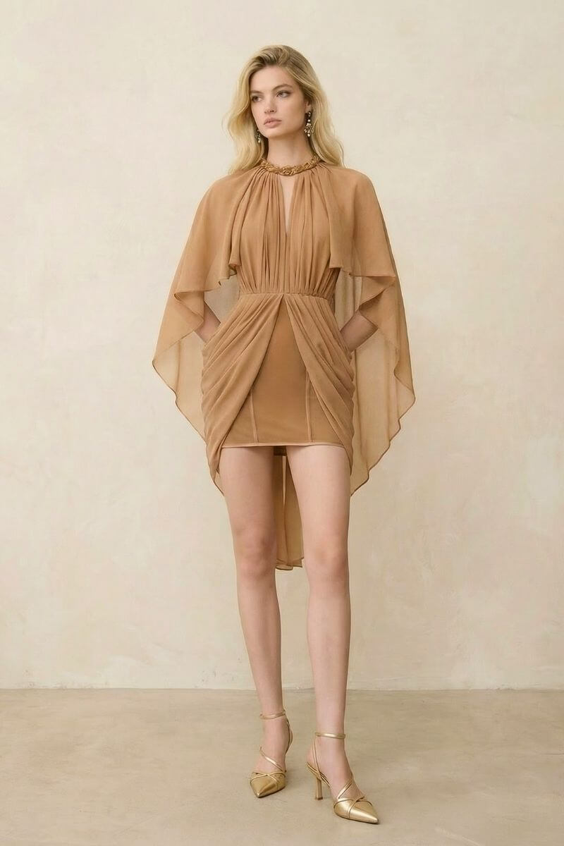Model wearing a camel chiffon mini dress featuring soft pleating, a draped front skirt, and airy cape sleeves, paired with gold heels for an elegant evening silhouette.