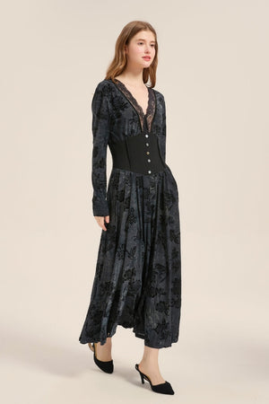 Model wearing a charcoal velvet maxi dress with deep V lace neckline, long sleeves, and structured corset waist panel with button accents.