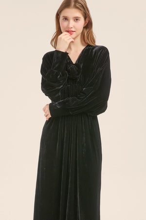 Model posing in a black velvet maxi dress with soft gathers and V-neckline, styled with loose hair and minimal makeup.