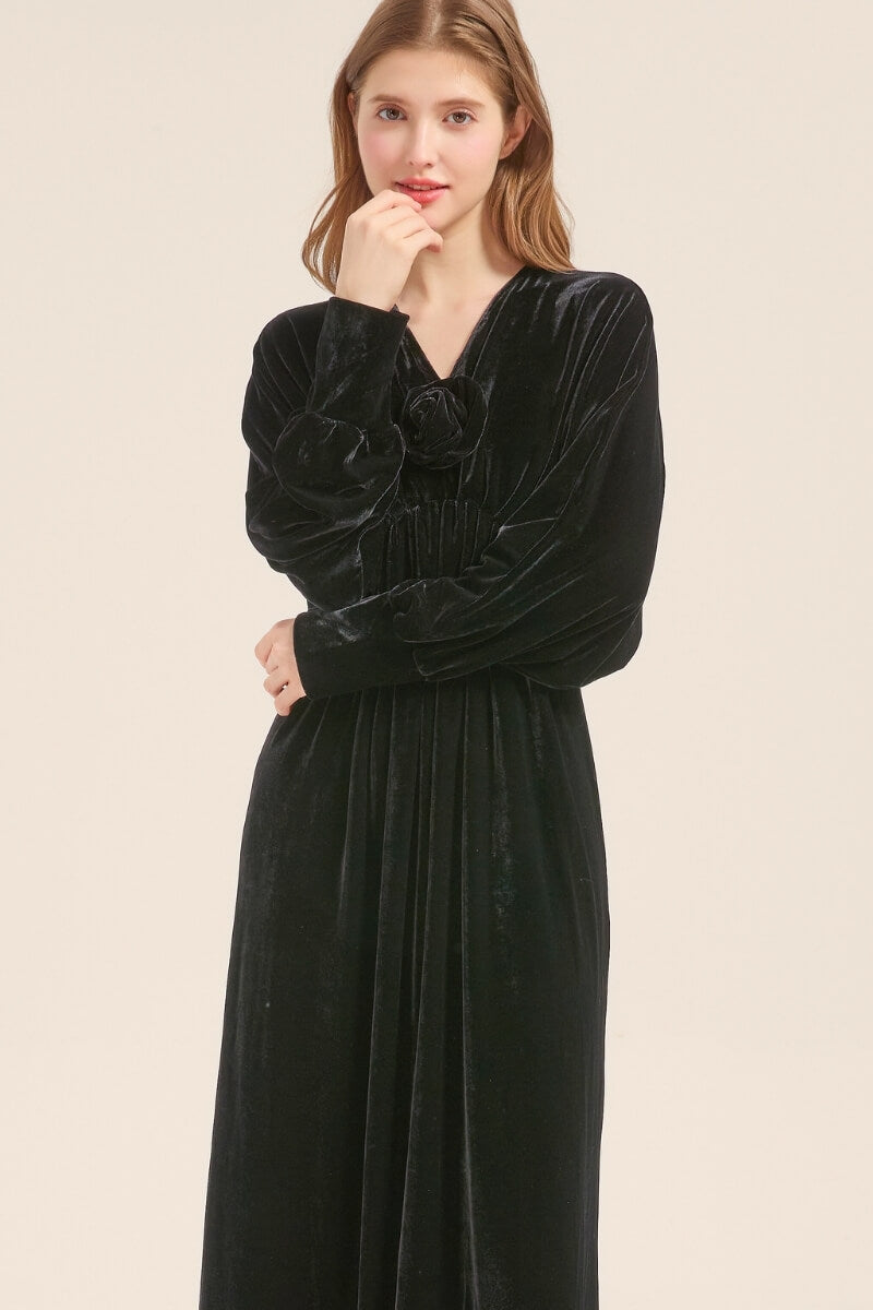 Model posing in a black velvet maxi dress with soft gathers and V-neckline, styled with loose hair and minimal makeup.