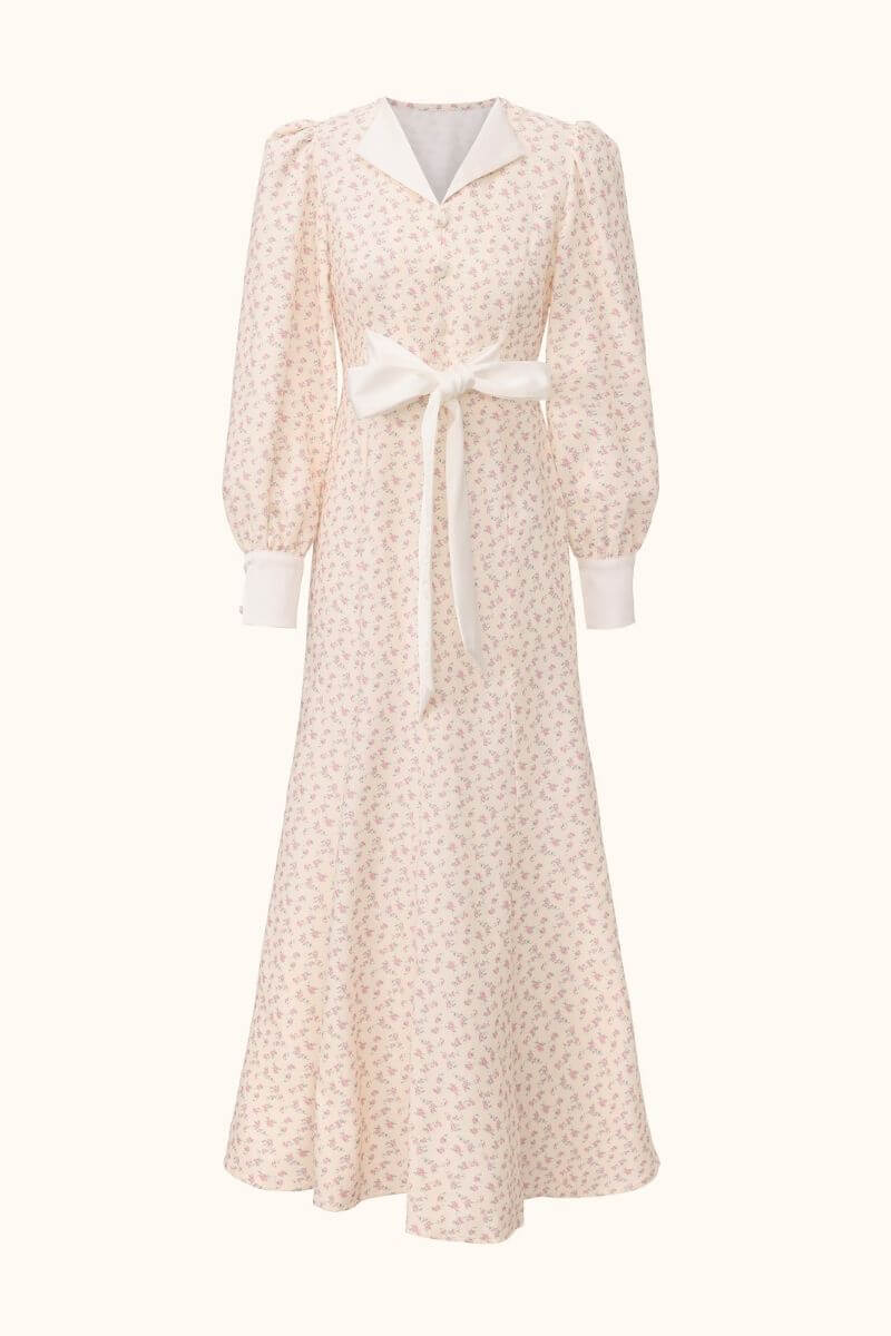 Front view of a cream midi dress with pink floral print, puff sleeves, white cuffs and collar, and a statement waist bow.