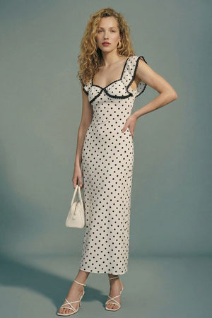 Model in a cream polka dot midi dress with black lace trim and flutter sleeves, captured at an angle to highlight the silhouette and delicate contrast details.
