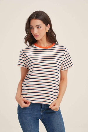 Front view of a woman in a cream striped tee featuring navy and orange lines and a contrast orange collar, paired with blue denim jeans for a relaxed everyday look.