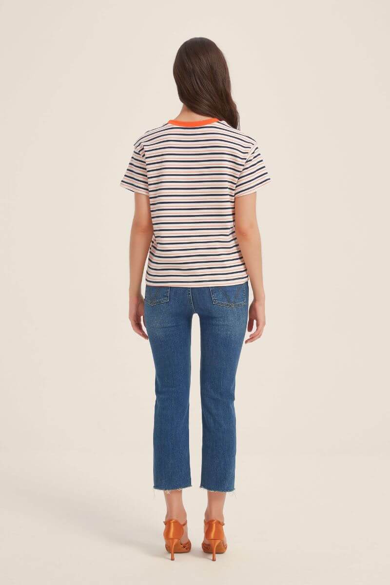 Back view of a cream T-shirt with navy and orange horizontal stripes and contrast orange neckline, styled with cropped blue jeans and orange heels.