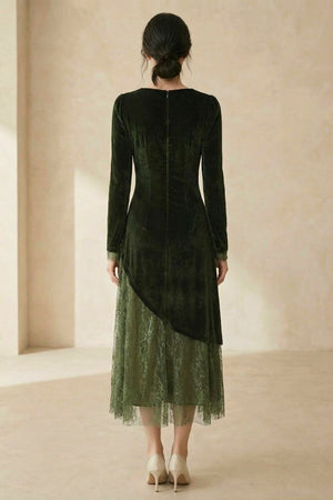 A woman shown from the back wearing a dark green velvet midi dress with an asymmetrical lace overlay hem, standing in a neutral indoor space.