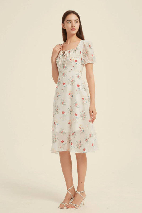 Full-length view of a floral square-neck midi dress with puff sleeves and flared hem, styled with white heels — soft feminine vintage style from Sioéne.