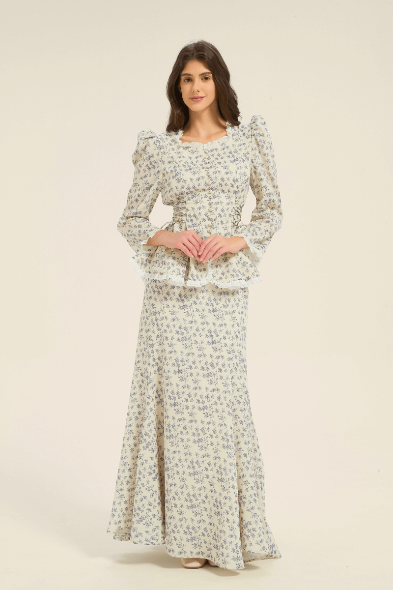 Model wearing a cream and blue floral two-piece set with long-sleeve peplum top and matching maxi skirt, front-facing view.