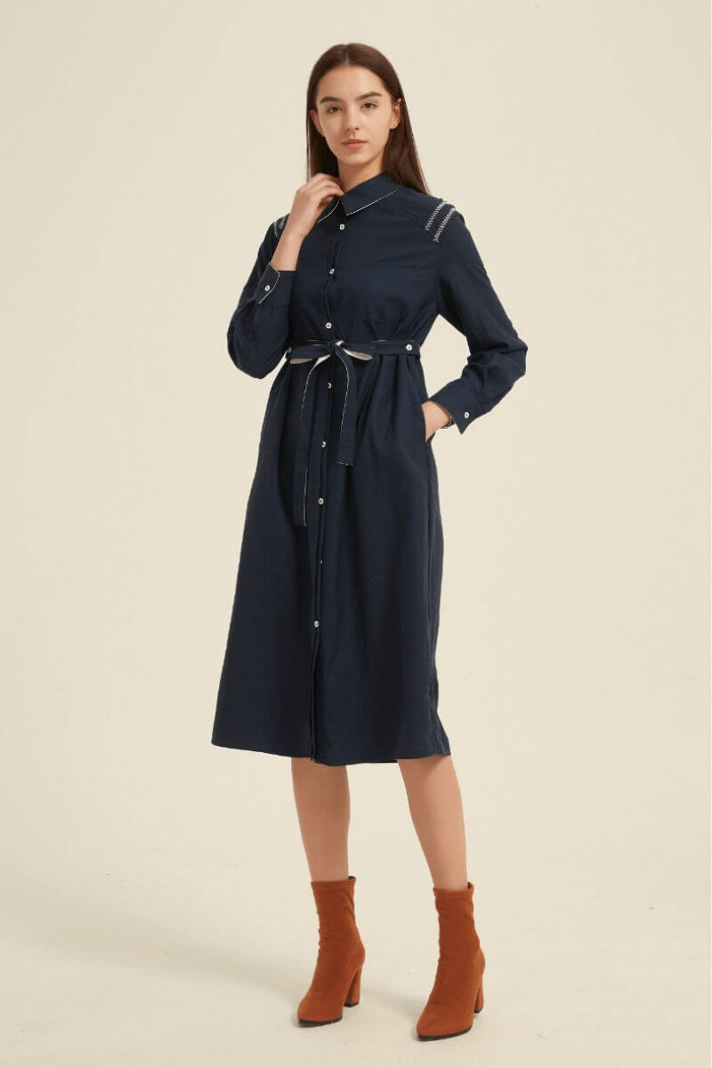 Model wearing a navy long-sleeve midi shirt dress with front buttons, collared neckline, and adjustable waist belt — refined everyday elegance.
