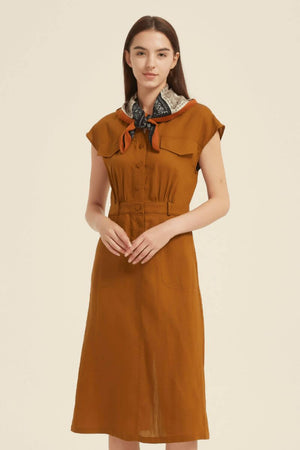 Model wearing a rust midi shirt dress styled with a paisley printed neck scarf, featuring a fitted waist and button-front closure — classic vintage-inspired elegance.