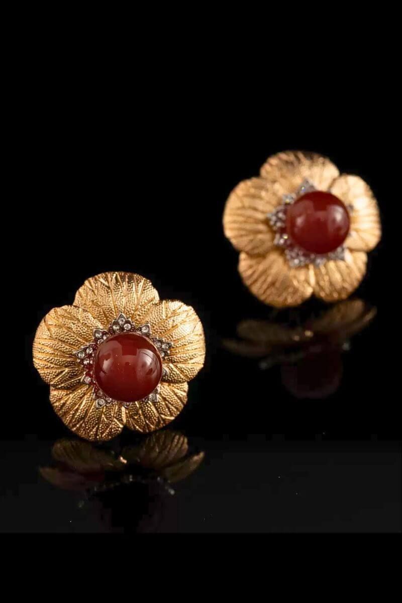 Gold floral stud earrings with a rich red carnelian center shown from a slight angle, highlighting the layered petal texture and reflective finish.