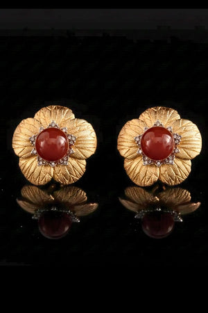 Two gold flower-shaped stud earrings featuring a domed red carnelian center and fine petal textures, arranged side by side on a black reflective background.