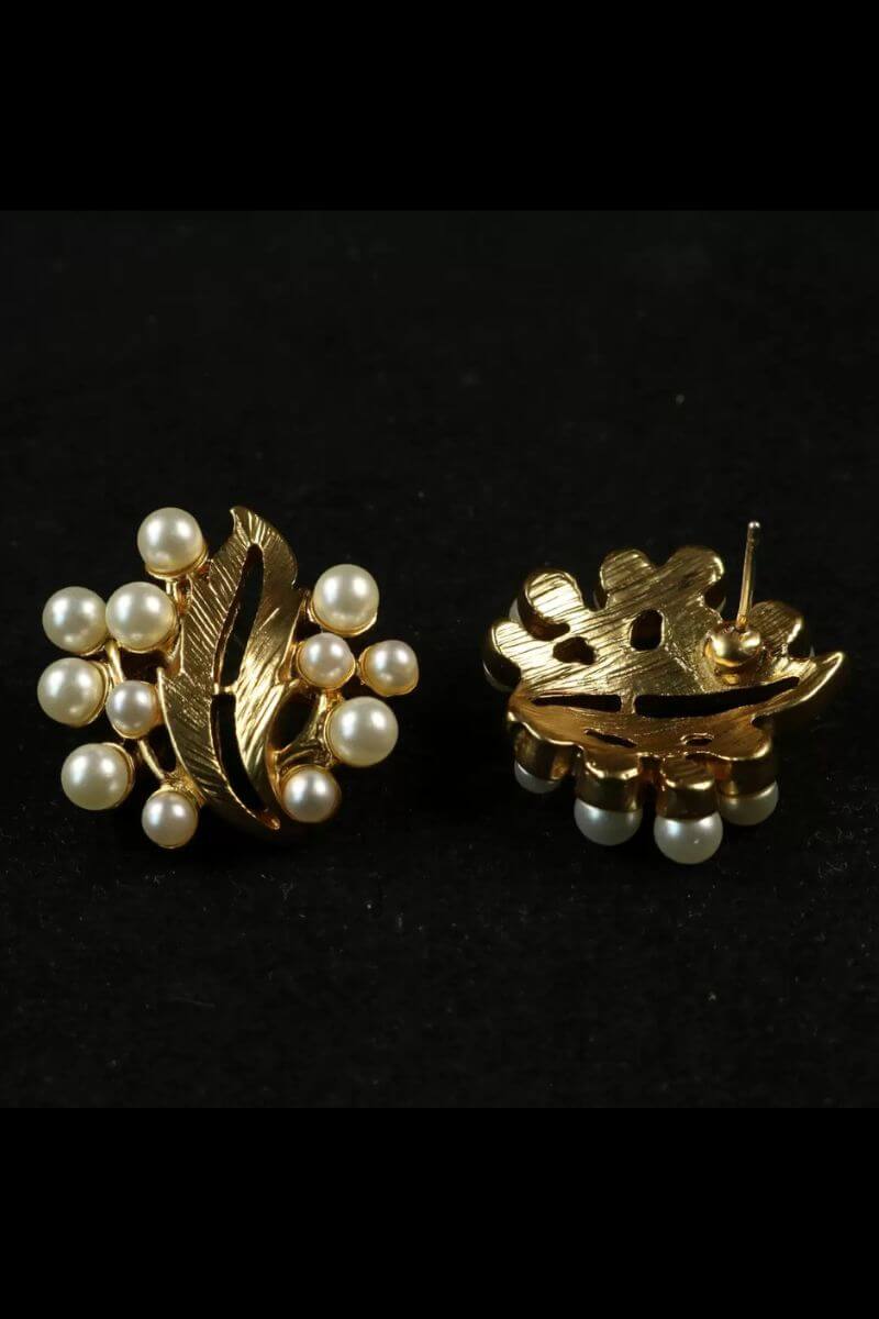 A close-up back view of a gold leaf–shaped stud earring featuring clustered round pearls, highlighting the sculpted metal texture and secure post backing against a black background.
