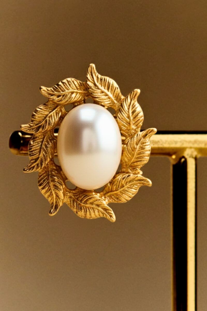 Close-up view of a gold leaf–textured stud earring centered with a smooth oval pearl, showcasing refined detailing and a timeless vintage feel.