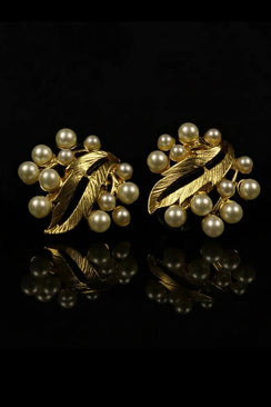 A pair of gold leaf–inspired pearl stud earrings arranged on a black reflective surface, showcasing the organic leaf form and softly luminous clustered pearls in a symmetrical display.