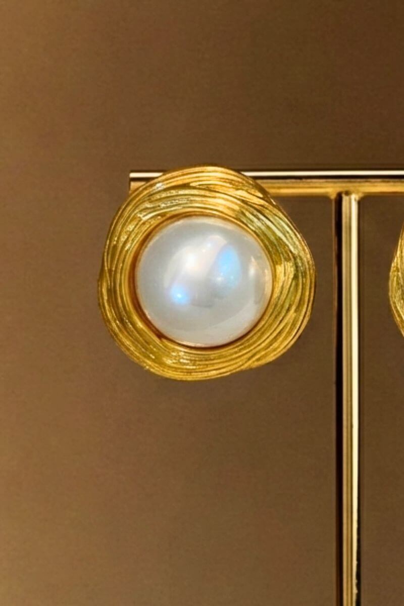 Close-up view of a gold swirl stud earring featuring a luminous round pearl set in a textured circular gold frame.
