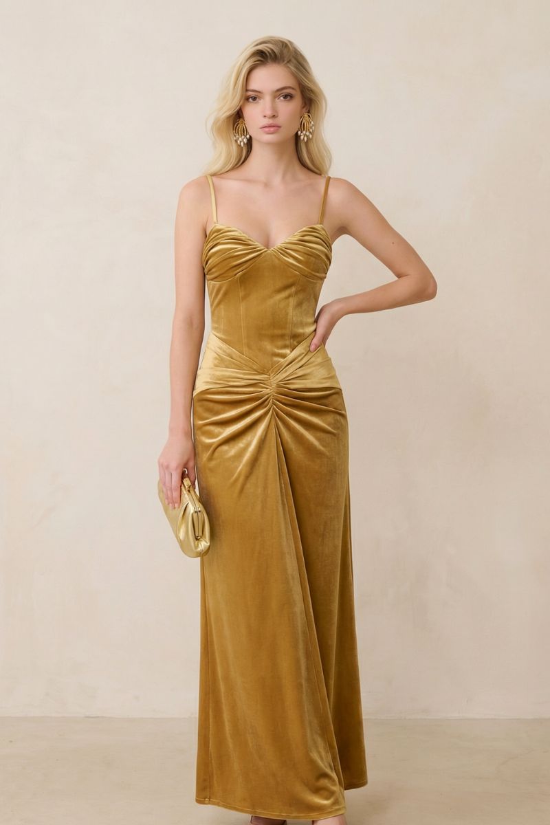 A blonde model wears a gold velvet ruched maxi dress with slim spaghetti straps and a softly draped waist, styled with gold statement earrings and a matching clutch.