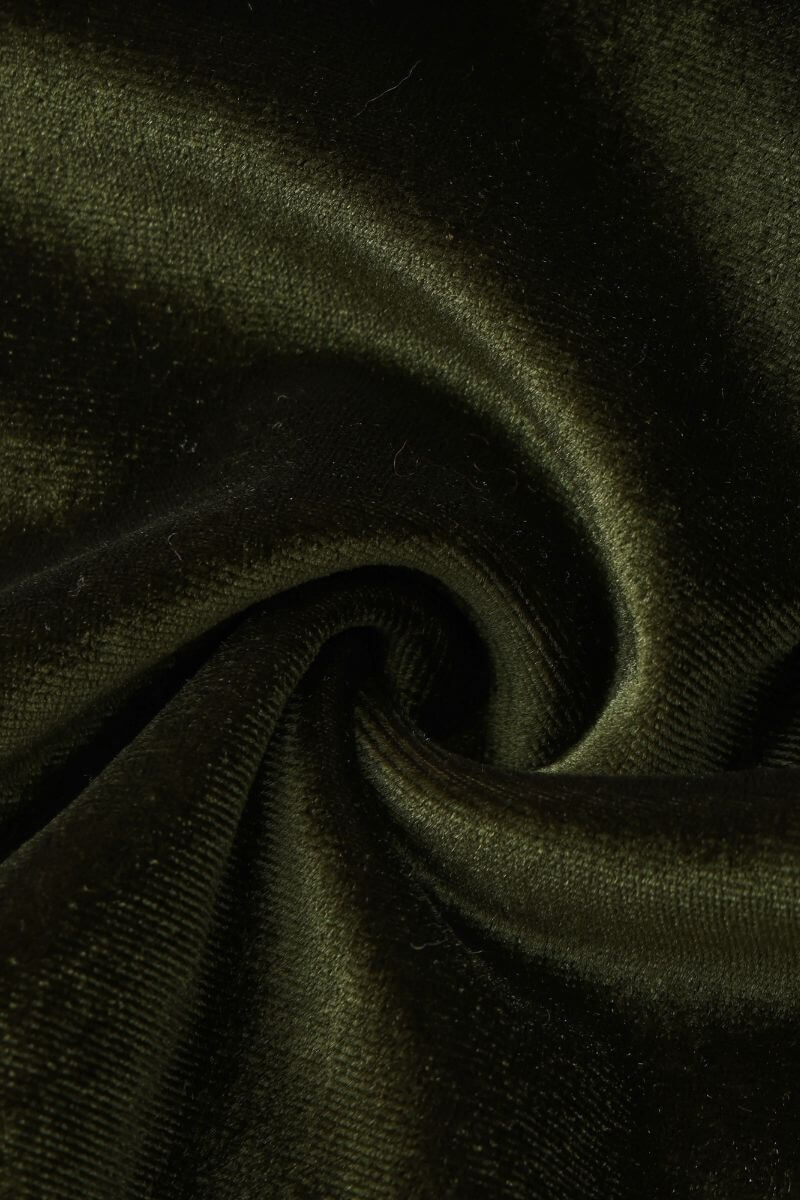 A close-up detail image of deep green velvet fabric showing its soft, plush texture and luxurious sheen in a twisted fold.