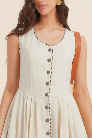 Close-up of a sleeveless ivory dress showing contrast black piping along the neckline and button placket, highlighting the textured fabric and elegant tailoring.