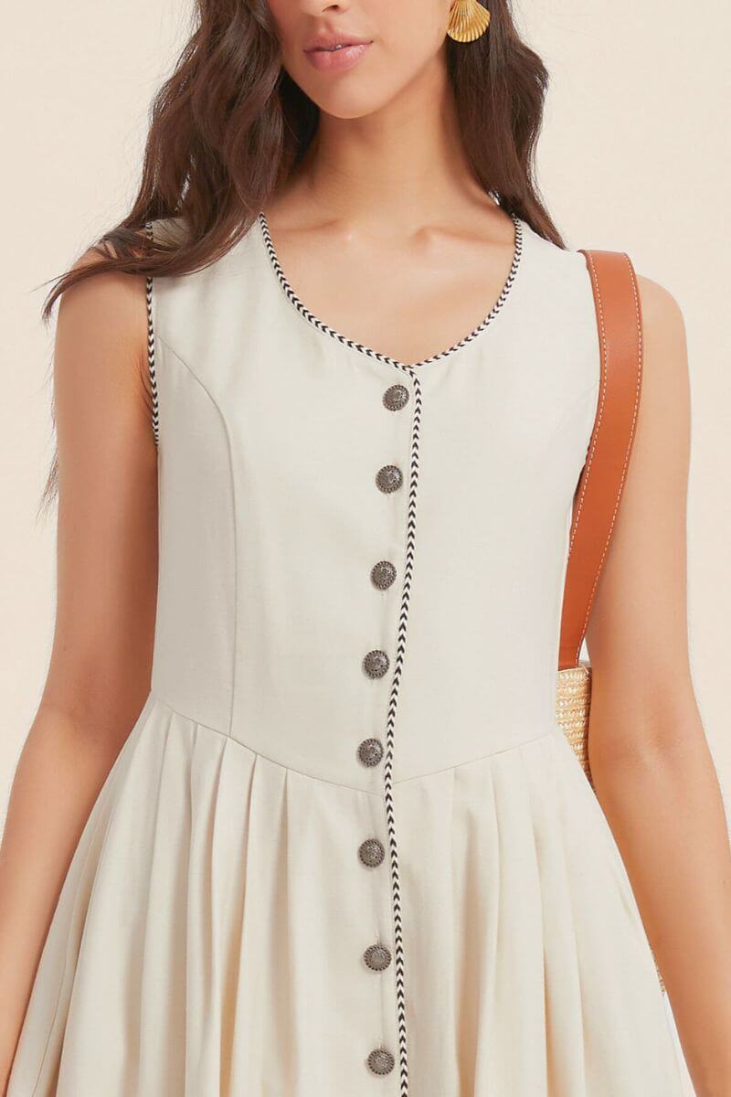 Close-up of a sleeveless ivory dress showing contrast black piping along the neckline and button placket, highlighting the textured fabric and elegant tailoring.