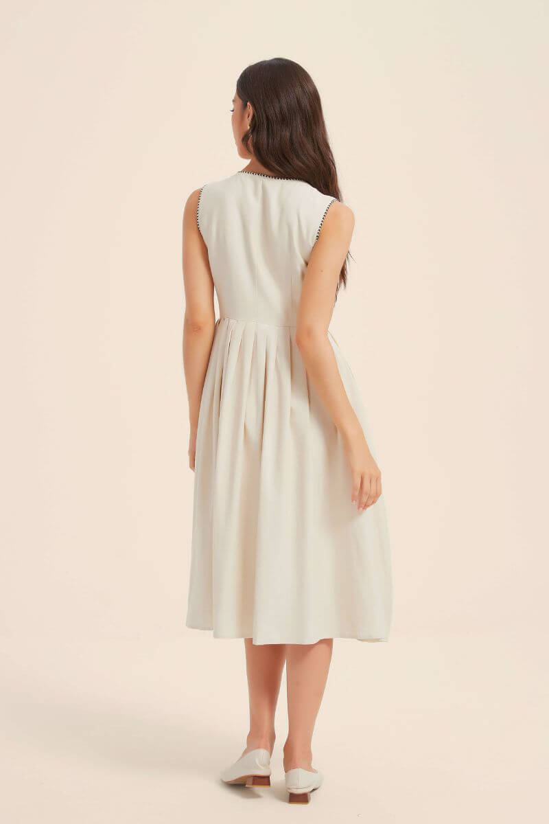 Back view of a sleeveless ivory button-down midi dress with a softly gathered waist and minimal silhouette, styled with white flats for a refined summer look.
