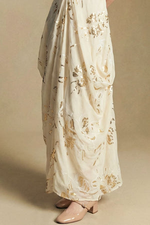 Close-up of the ivory maxi dress fabric showing delicate gold sequin floral embroidery and soft draping movement around the skirt.