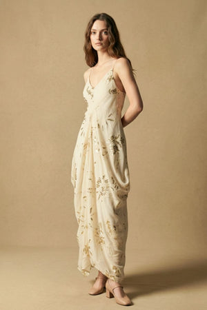 Side profile of a model wearing an ivory maxi dress with gold sequin floral details, highlighting the fluid drape and elongated silhouette.