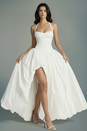 Model lifts the skirt of an ivory halter corset maxi dress to reveal its airy volume and fluid drape, emphasizing the romantic movement of the design.