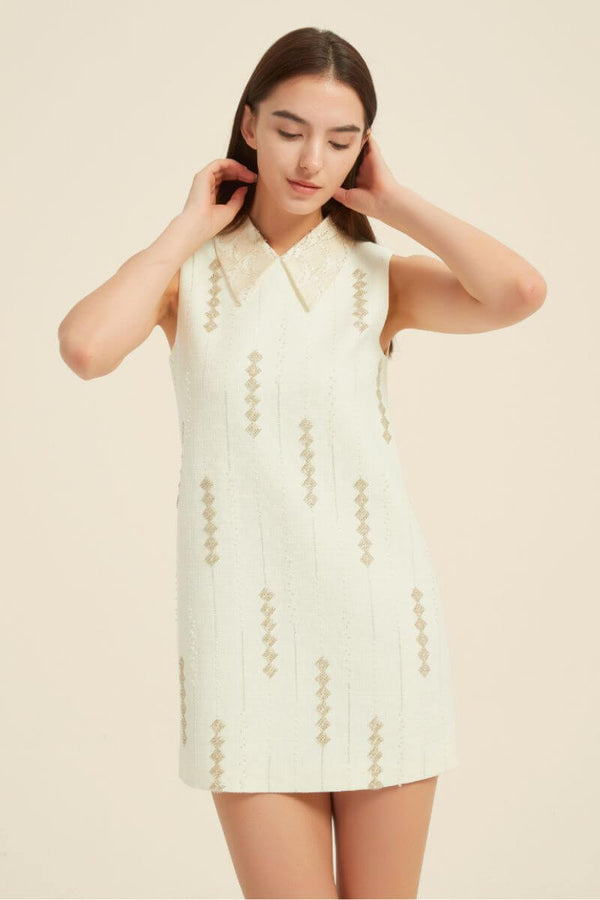 Model wearing an ivory sleeveless mini dress with lace collar and vertical gold sequin embroidery in a vintage-inspired design.