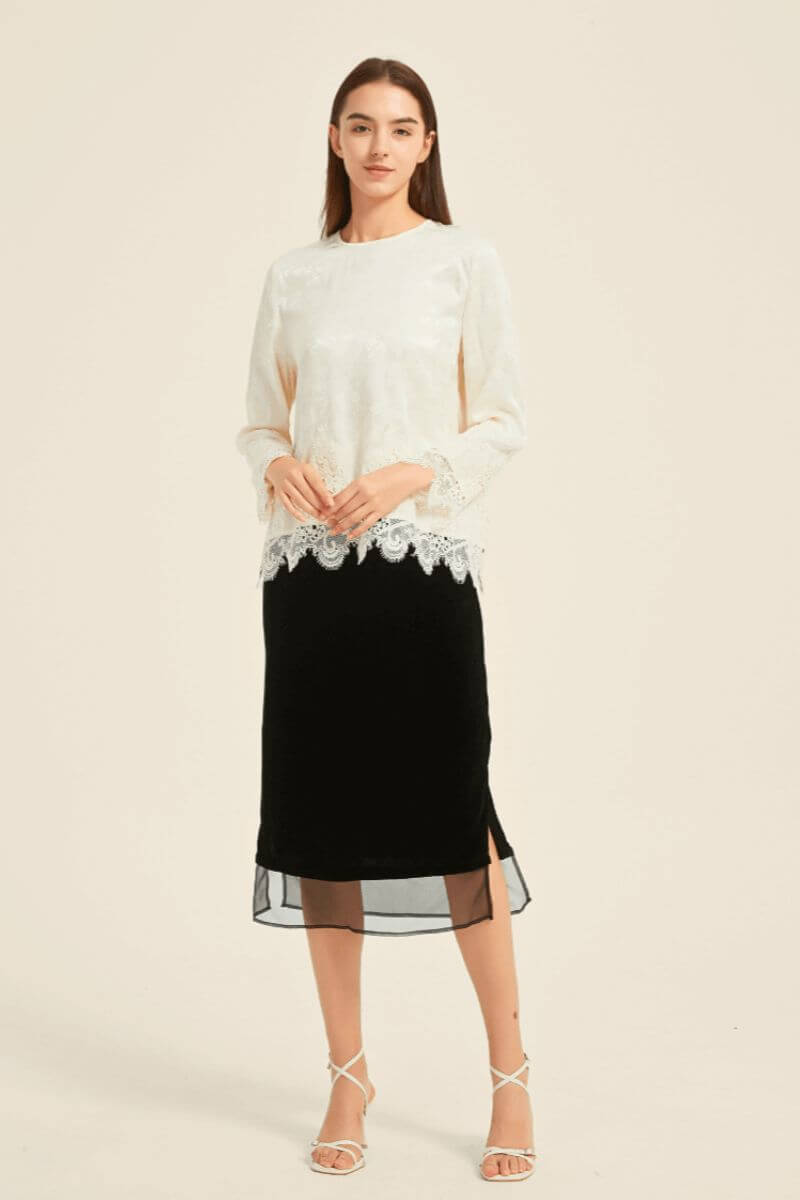 Model wearing an ivory lace-trim blouse paired with a black sheer-hem midi skirt and white strappy heels — elegant monochrome outfit styled by Sioéne.