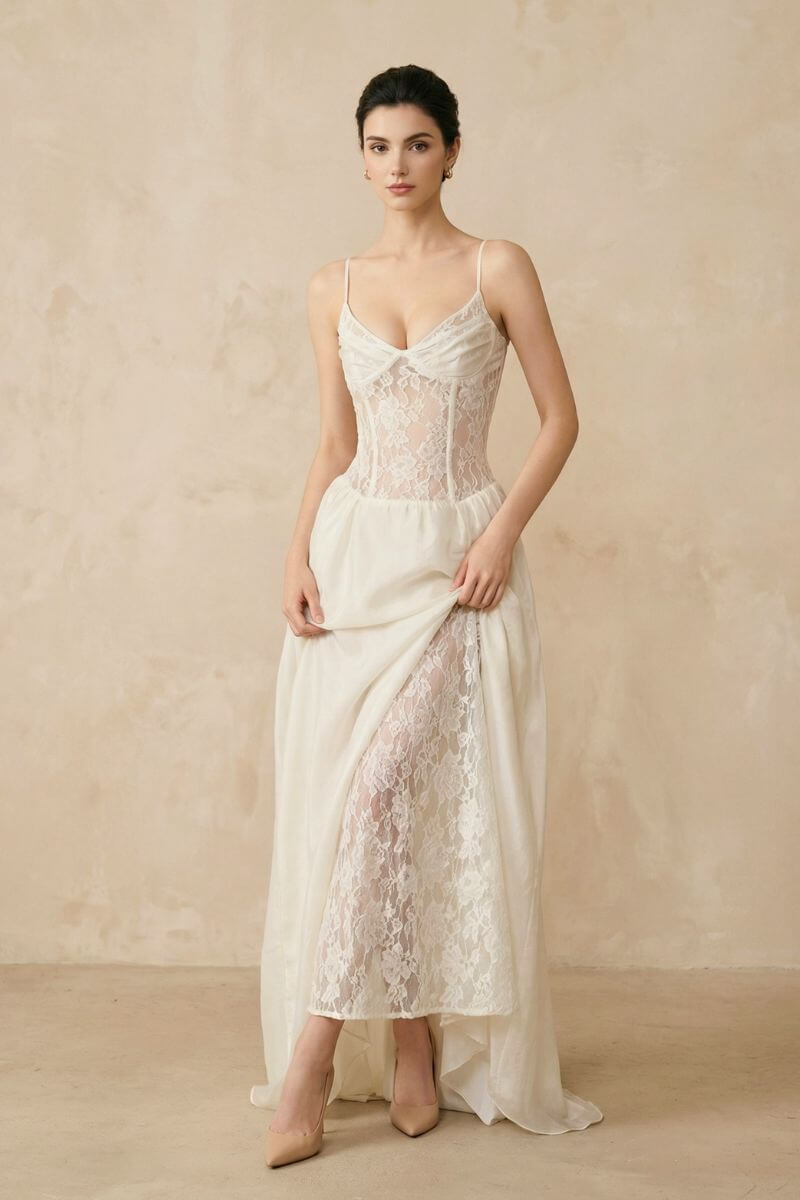 A model showcases an ivory lace corset maxi dress with a sheer lace bodice and front slit, styled with nude heels against a warm neutral studio backdrop.