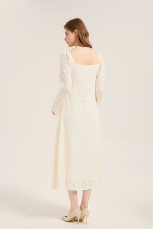 Model turned to show the back of an ivory lace midi dress with square neckline and fitted lace pattern throughout, styled with beige heels.