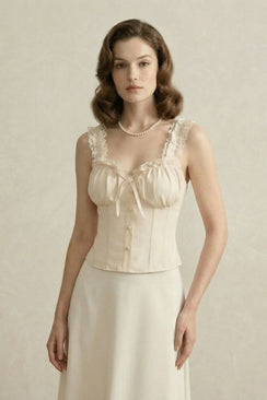 Close-up of a model wearing an ivory lace-trim corset top with gathered bust and pearl necklace in a beige backdrop.