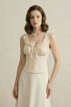 Close-up of a model wearing an ivory lace-trim corset top with gathered bust and pearl necklace in a beige backdrop.